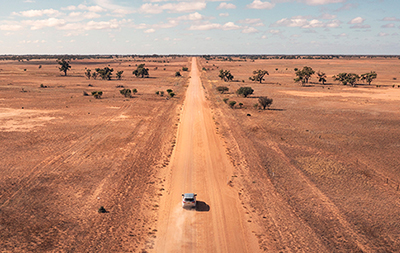Aerial overlooking a vehicle driving along outback road. Credit: Destination NSW