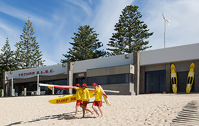 Surf lifesavers carrying surfboards on beach at Tathra Surf Club. Credit: Destination NSW
