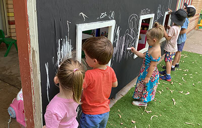 Line of children using chalk on blackboard at upgraded Coonamble Children Services