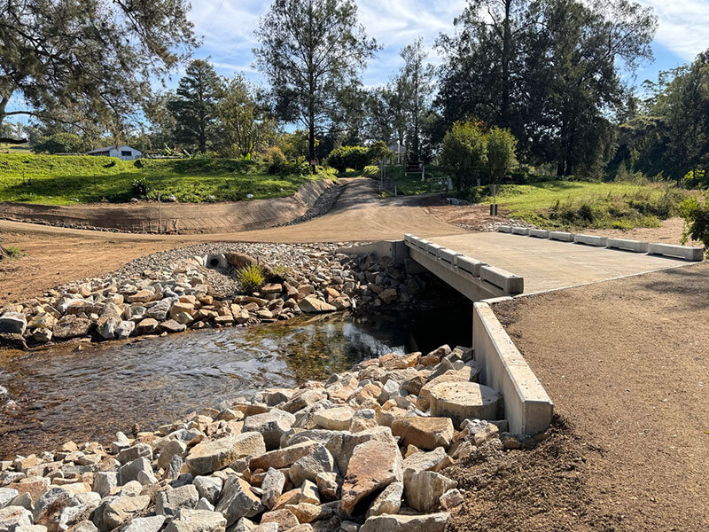Concrete bridge over creek with large rocks on side.