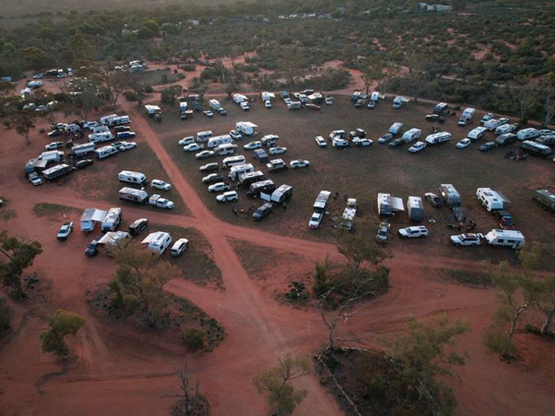 Aerial view of many cars parked on red dirt at the Mundi Mundi Bash in Broken Hill.