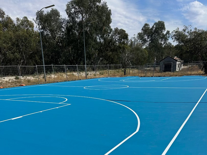 A newly refurbished tennis court. The court is caged and there are trees in the background.