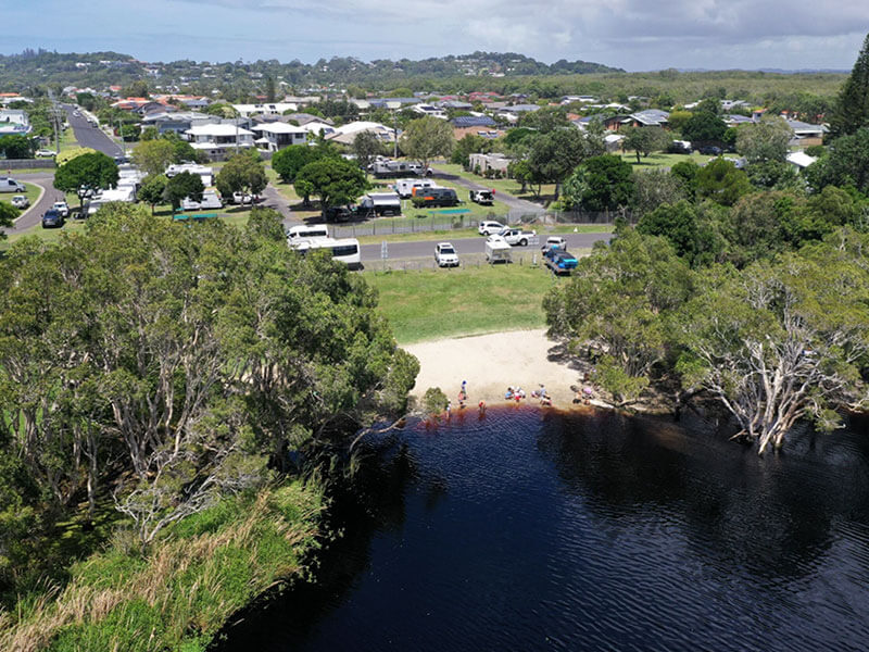 Aerial view sandy beach of Lake Ainsworth with caravan park in background.