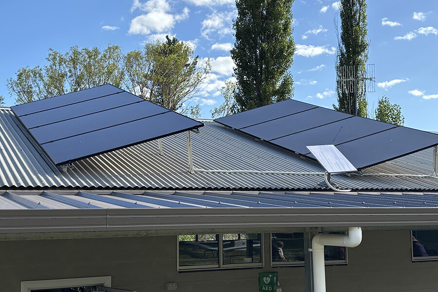 Solar panels on a corrugated iron roof at a new building. There are trees in the background and 